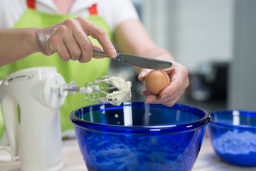 Eine Hausfrau bereitet Waffelteig zu. Sie schl&auml;gt ein Ei mit einem Messer auf um es in die Teigsch&uuml;ssel zu geben.