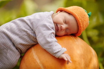 baby with pumpkin hat sleeping on big orange pumpkin