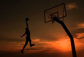 Young man is playing basketball during sunset