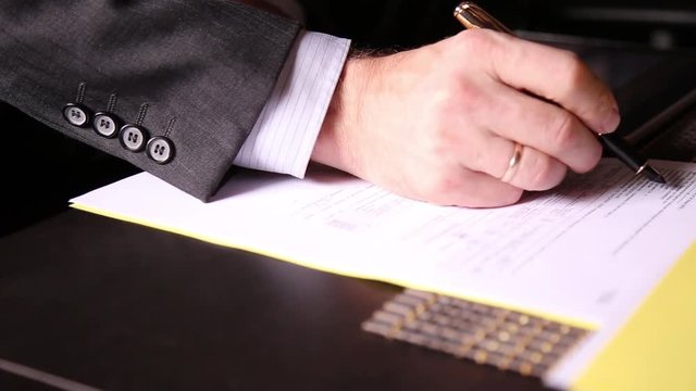 Businessman sitting office desk signs a bill comparing them, with the pc tablet. close-up hands of a man and a fountain pen