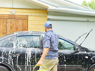 Man washing his black car near house.