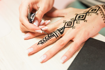 young woman mehendi artist painting henna on the hand