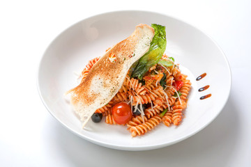 Pasta in tomato sauce with fried green beans and the pods of young peas, sweet peppers,with fresh feta cheese and cherry tomatoes and olives in a white deep bowl.