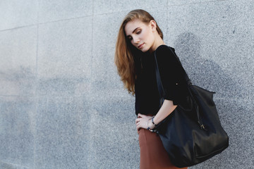 Fototapeta premium Beautiful woman wearing black blouse, brown pencil skirt and high heels shoes with leather bag posing at the evening city street. Vogue, female model 