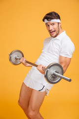 Amusing young sportsman shouting and holding heavy barbell