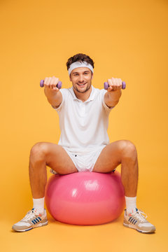 Sportsman man on fitness ball doing exercises with small dumbbells