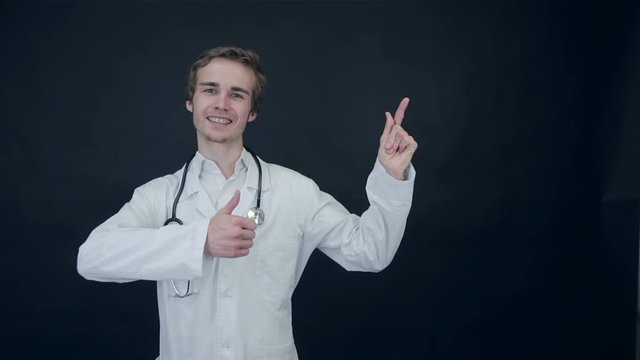 Smiling Doctor showing thumbs up, standing on a black background. Packshot. HD.