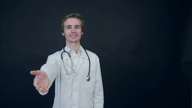 Smiling Doctor giving a hand for help, standing on a black background. Packshot. HD.