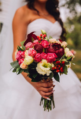 Close up of wedding bouquet of bridal flowers in hands of anonymous bride. Focus on fresh red flowers.