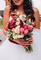 Close up of wedding bouquet of bridal flowers in hands of anonymous bride. Focus on fresh red flowers.