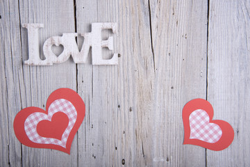 Word LOVE and paper hearts on old wooden background