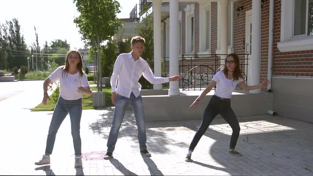 Three girls and boy dressed in similar jeans and shirts dancing in the street HD