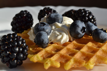 Homemade waffles with fresh blueberry, blackberry and whipped cream. Sweet pastry and fresh fruits - tasty summer breakfast. Close up.