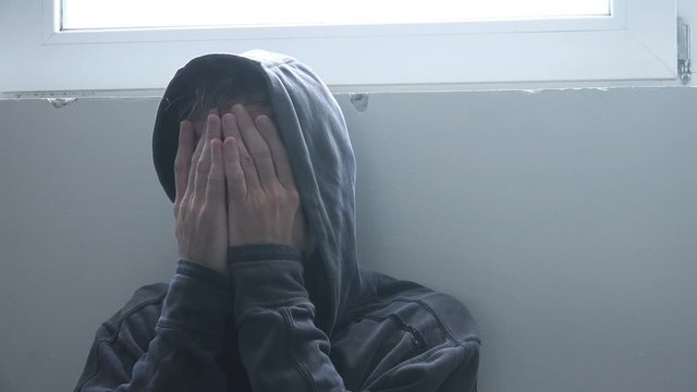 Drug addiction problems, hooded adult male having abstinence crisis, hands covering face in despair