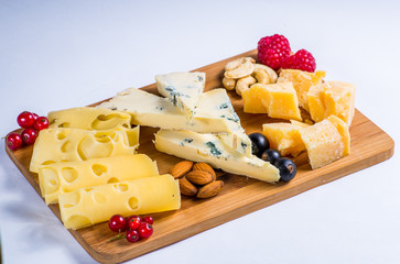 pieces of cheese on a wooden board served with berries and nuts