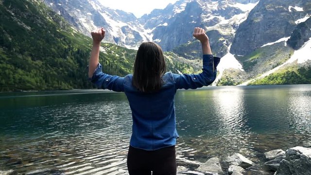 Young woman raising arms close to the lake in the country mountains, slow motion 240fps
