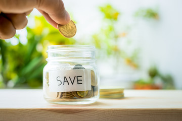 Hand putting money coin in glass jar with save word.For savings