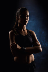 Beautiful sportive girl posing with crossed arms over dark background.