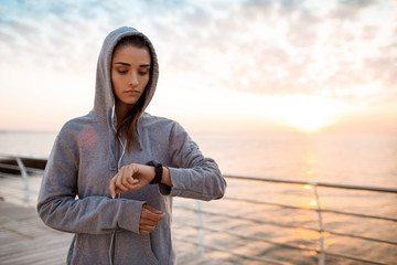 Beautiful sportive girl looking at watch during sunrise over seaside.