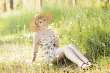 Young woman wearing sundress and hat while sitting among the flowers in the woods.