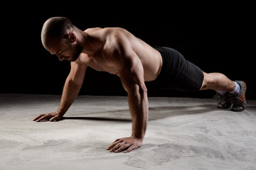 Young powerful sportsman training push ups over dark background.