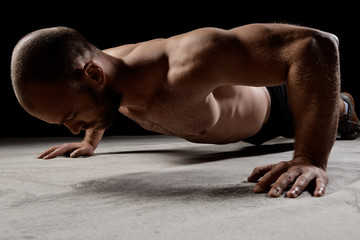Obraz premium Young powerful sportsman training push ups over dark background.