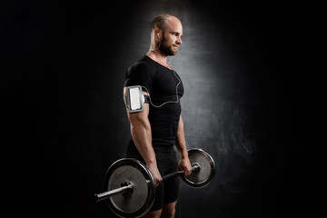 Young powerful sportsman training with barbell over black background.