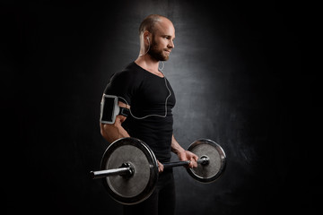 Fototapeta na wymiar Young powerful sportsman training with barbell over black background.