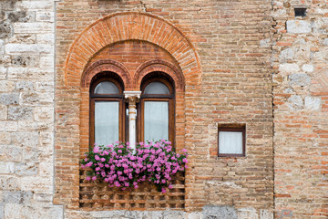 Fototapeta na wymiar Ancient window with flowers in the medieval town San Gimignano in Tuscany, Italy.