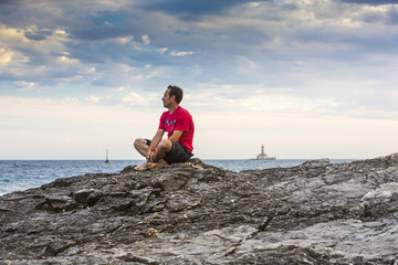 Fototapeta na wymiar Kroatien, Istrien, Kap Kamenjak, Mann sitzt auf den Felsklippen und schaut entspannt auf die Brandung