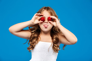 Young pretty girl hiding eyes with strawberry over blue background.