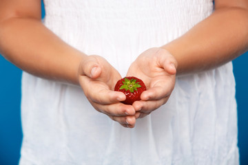 Close up of girl's hand holding strawberry over blue background.