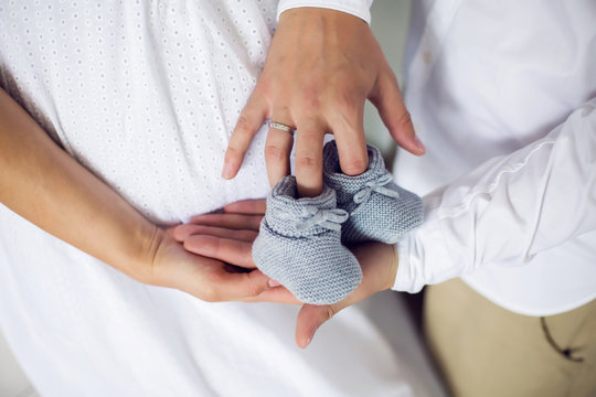 hands of their parents, dressed in white, holding a knitted blue booties
