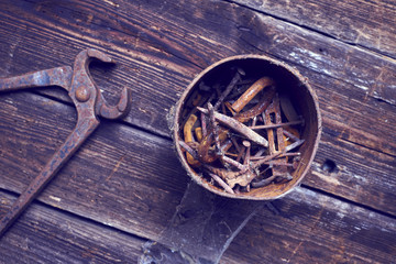 old rusty pinchers with can of nails on wooden boards background
