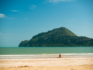 Toned image of a woman sits on the beach during low tide on the background of the islands with trees and sky with clouds
