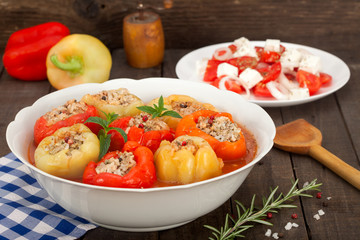 Stuffed bell peppers with spicy tomato sauce and rosemary in a dish on the rustic wooden background