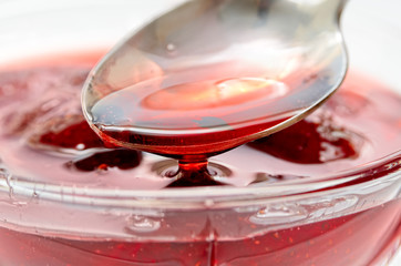 Strawberry jam is stirred with a spoon on a white background. Fruit dessert close up. Confectionery.