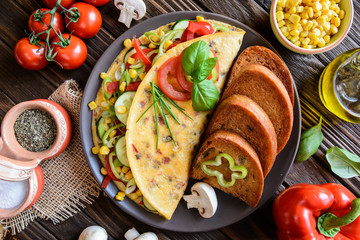 Omelet with pepper, tomato, corn, green onion, cucumber, mushrooms and fried bread on a wooden background