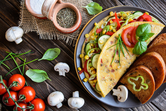 Omelet with pepper, tomato, corn, green onion, cucumber, mushrooms and fried bread on a wooden background