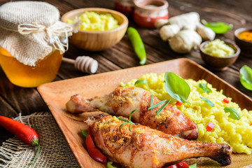 Baked chicken thighs with honey, grated ginger and rice with turmeric on a wooden background