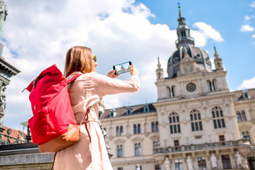 Young woman photographing with phone town hall building in Graz old town. Traveling in Austria
