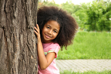 Afro-American little girl hiding behind tree in park