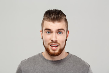 Fototapeta premium Surprised young handsome man posing over grey background. Copy space.