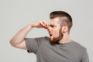 Young handsome man pinching nose over grey background. Copy space. 