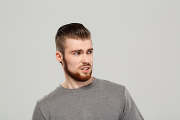 Upset young handsome man posing over grey background. Copy space.