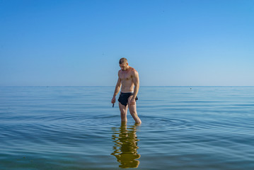 A man in a loincloth standing in water with a knife in his hand.