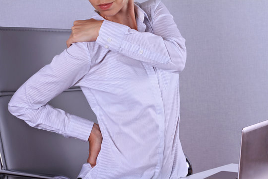 Business Woman Suffering From Back Pain At Desk In Office. Pain Relief Concept