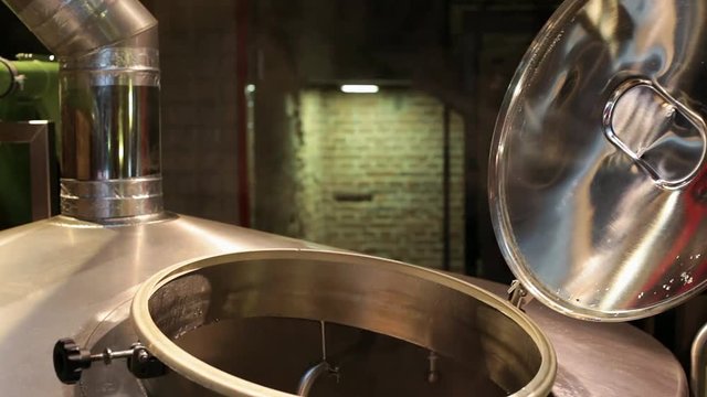 Steam is coming from stainless stell tank during beer brewing process in  in the brewery. 