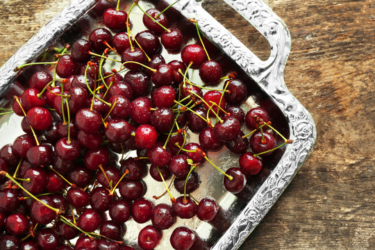 Old metal tray with ripe cherries on wooden background