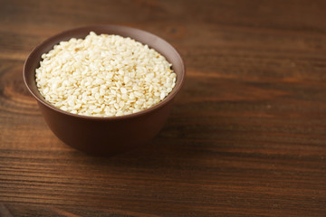 Bowl with white sesame on wooden background